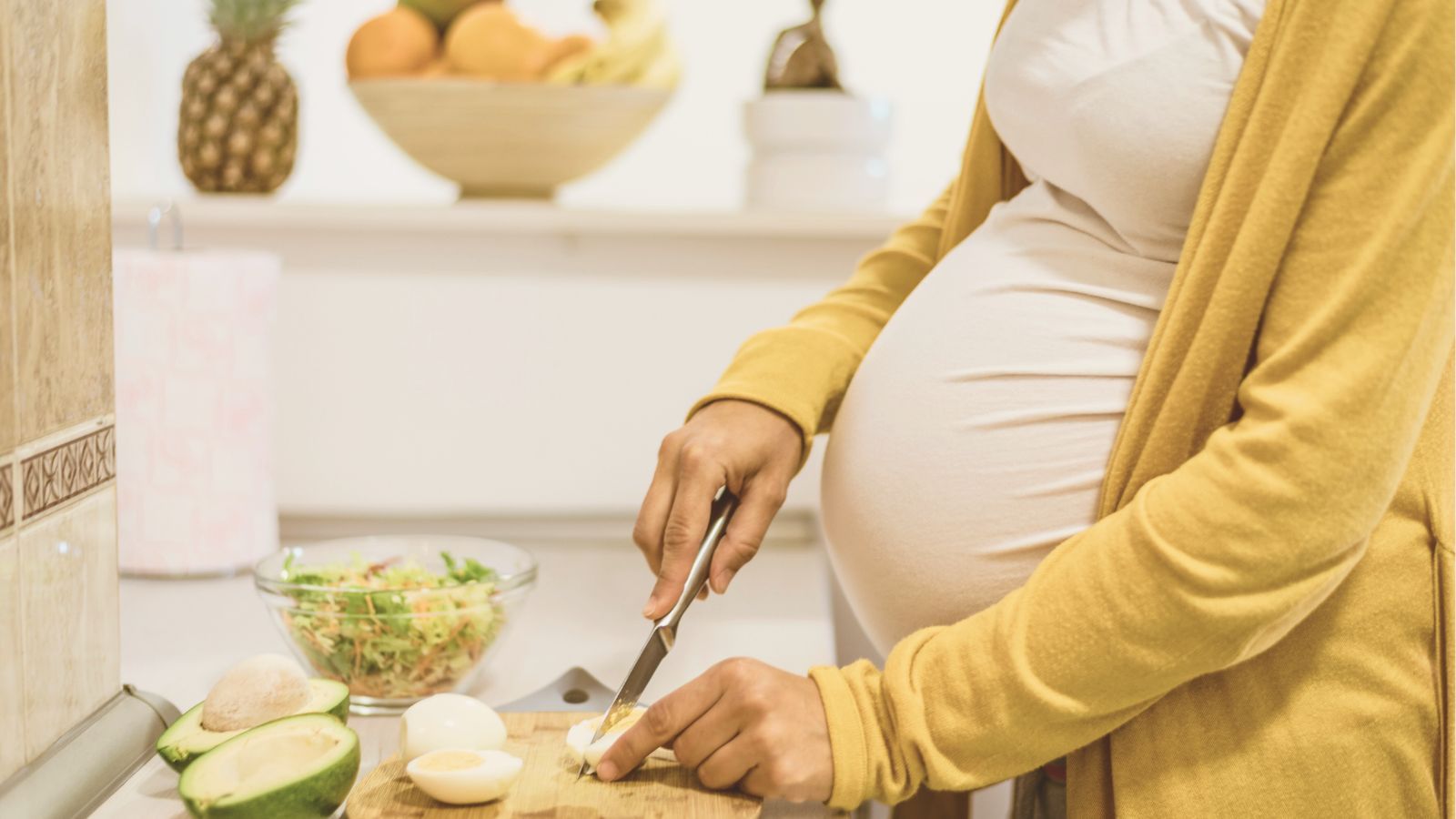 Mujer embarazada cortando un huevo y aguacate en la cocina, preparando una comida saludable